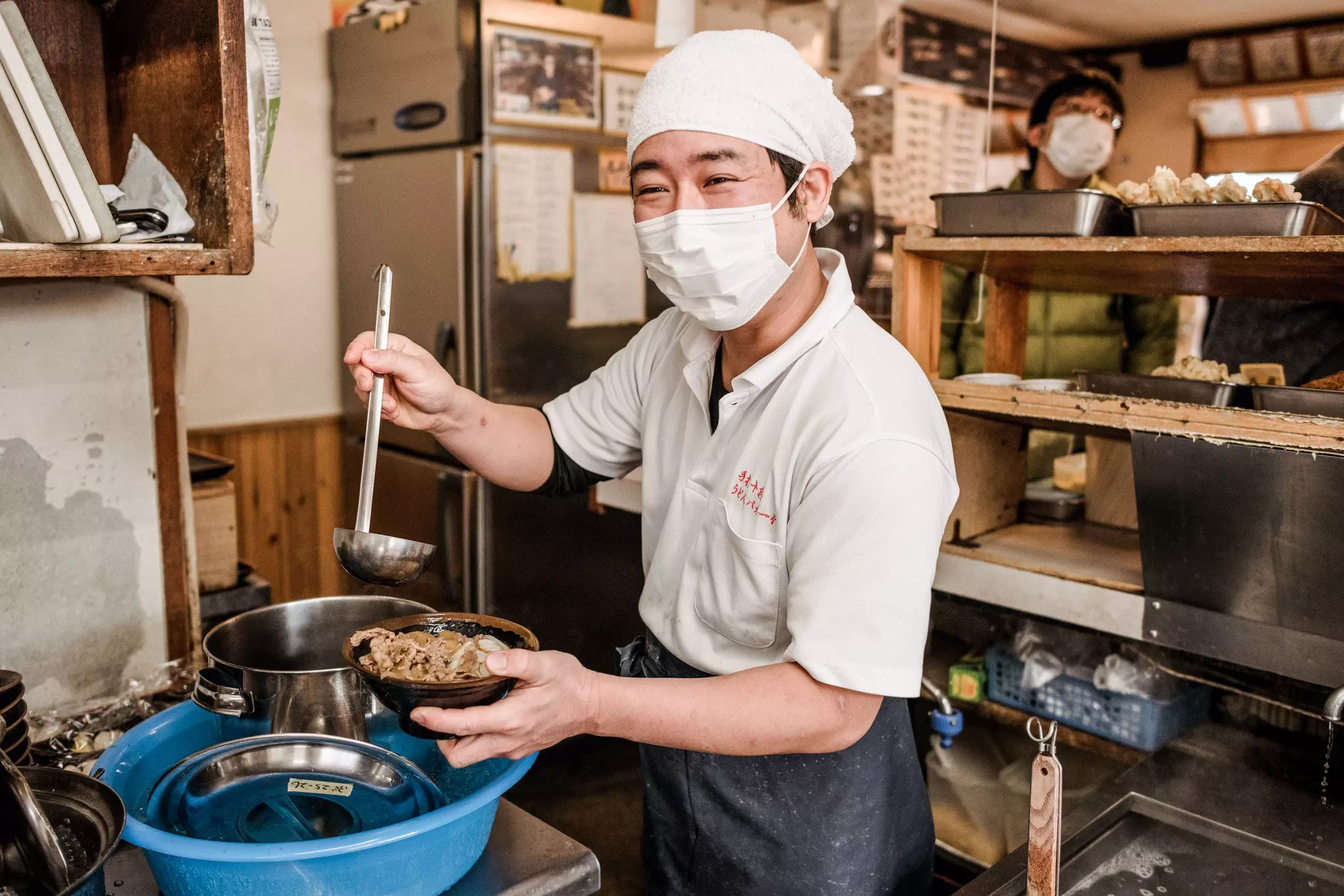 A chef preparing a bowl of udon noodles in a commercial kitchen.