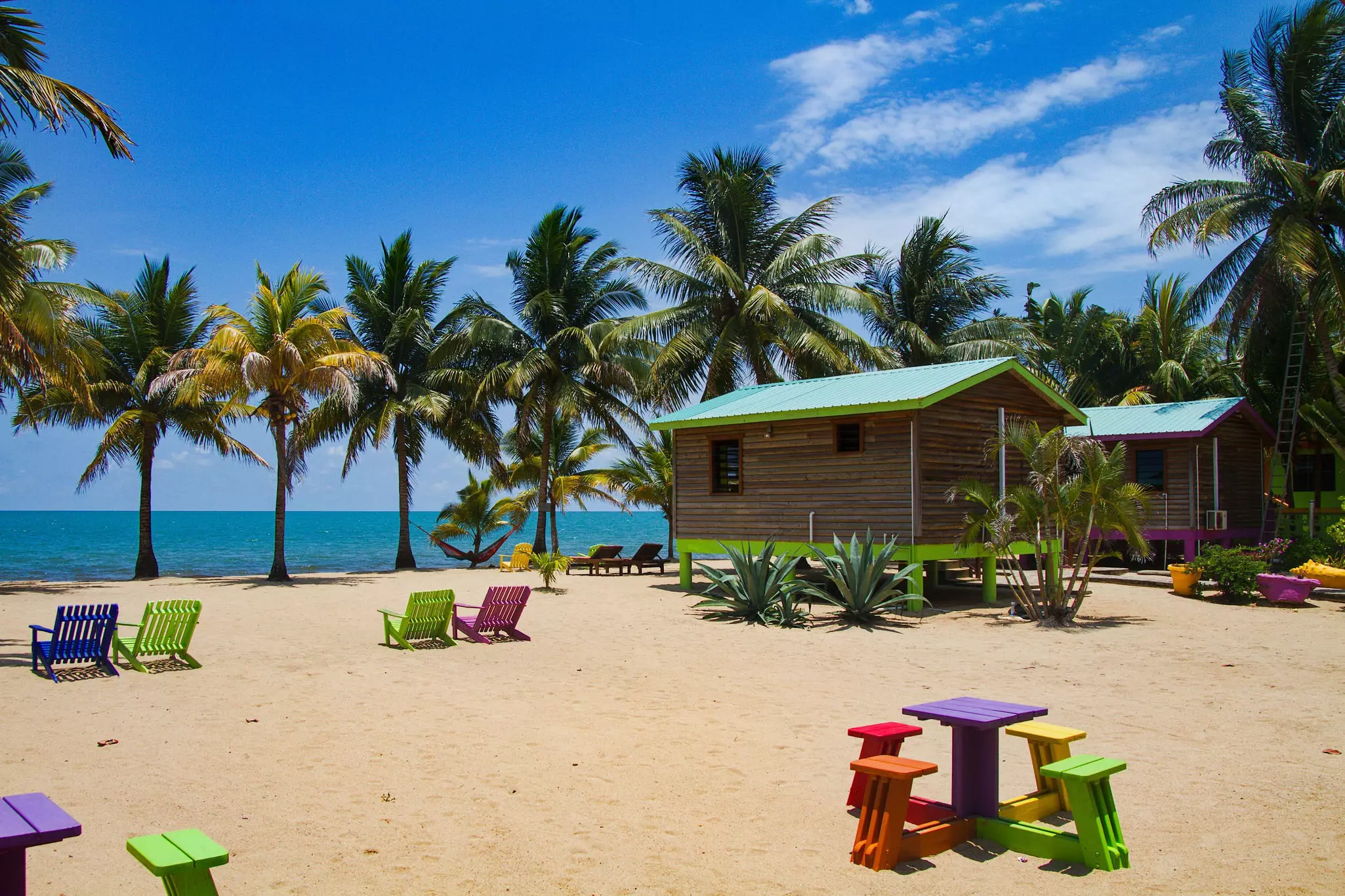 A wooden cabin on stilts on a sandy beach.