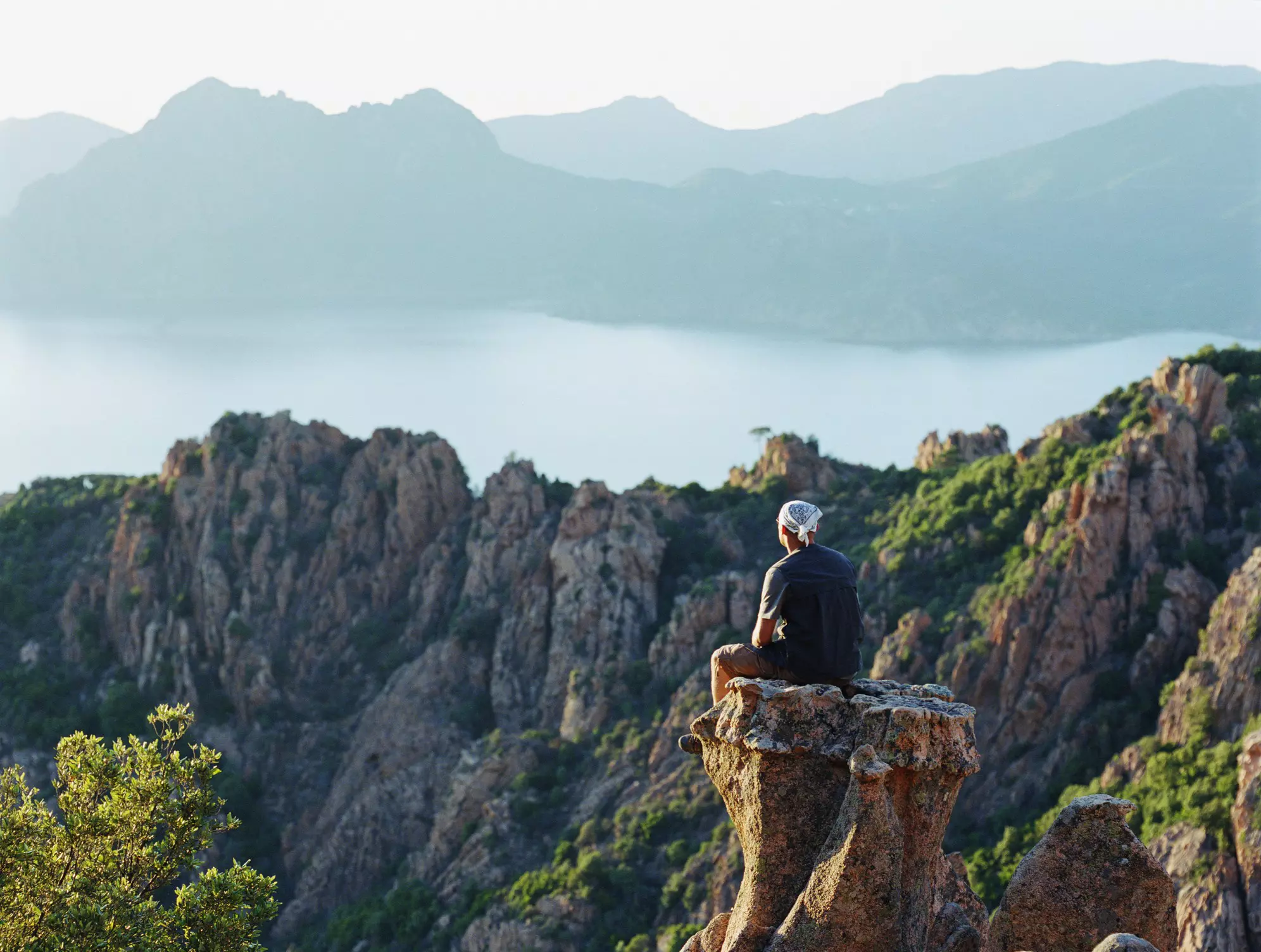 Man sitting on a rocky peak in Le Calanques de Piana, Gulfe de Porto, Corsica