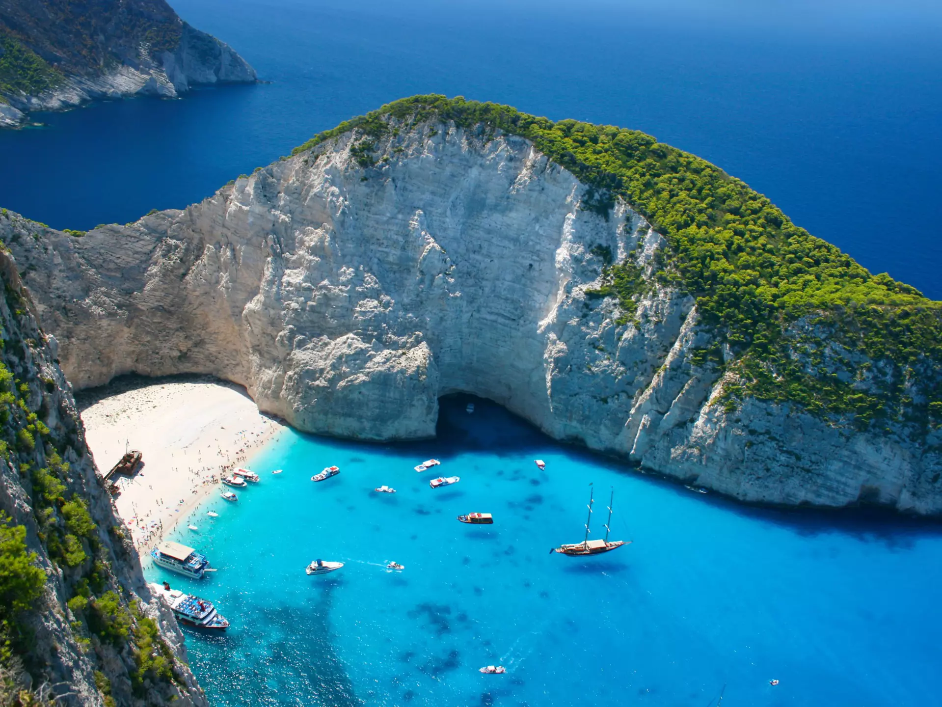 An overhead view of an island beach by dramatic cliffs, surrounded by blue waters