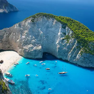 An overhead view of an island beach by dramatic cliffs, surrounded by blue waters