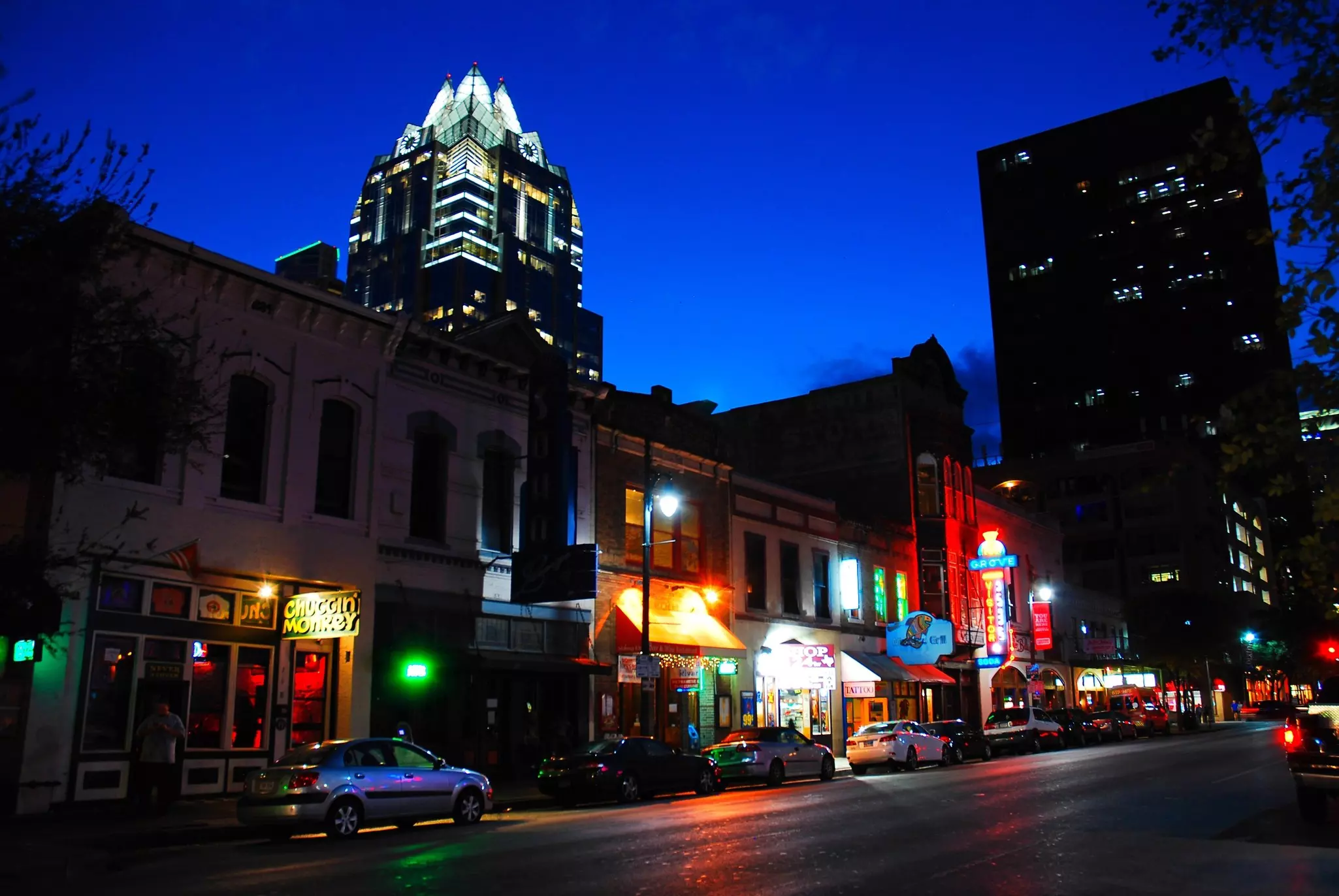 The colored lights in front of restaurants and bars on a city street are illuminated at dusk.