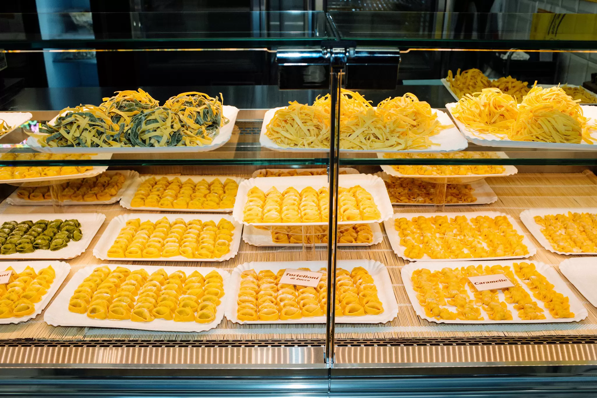 A glass display case with many types of fresh pasta.