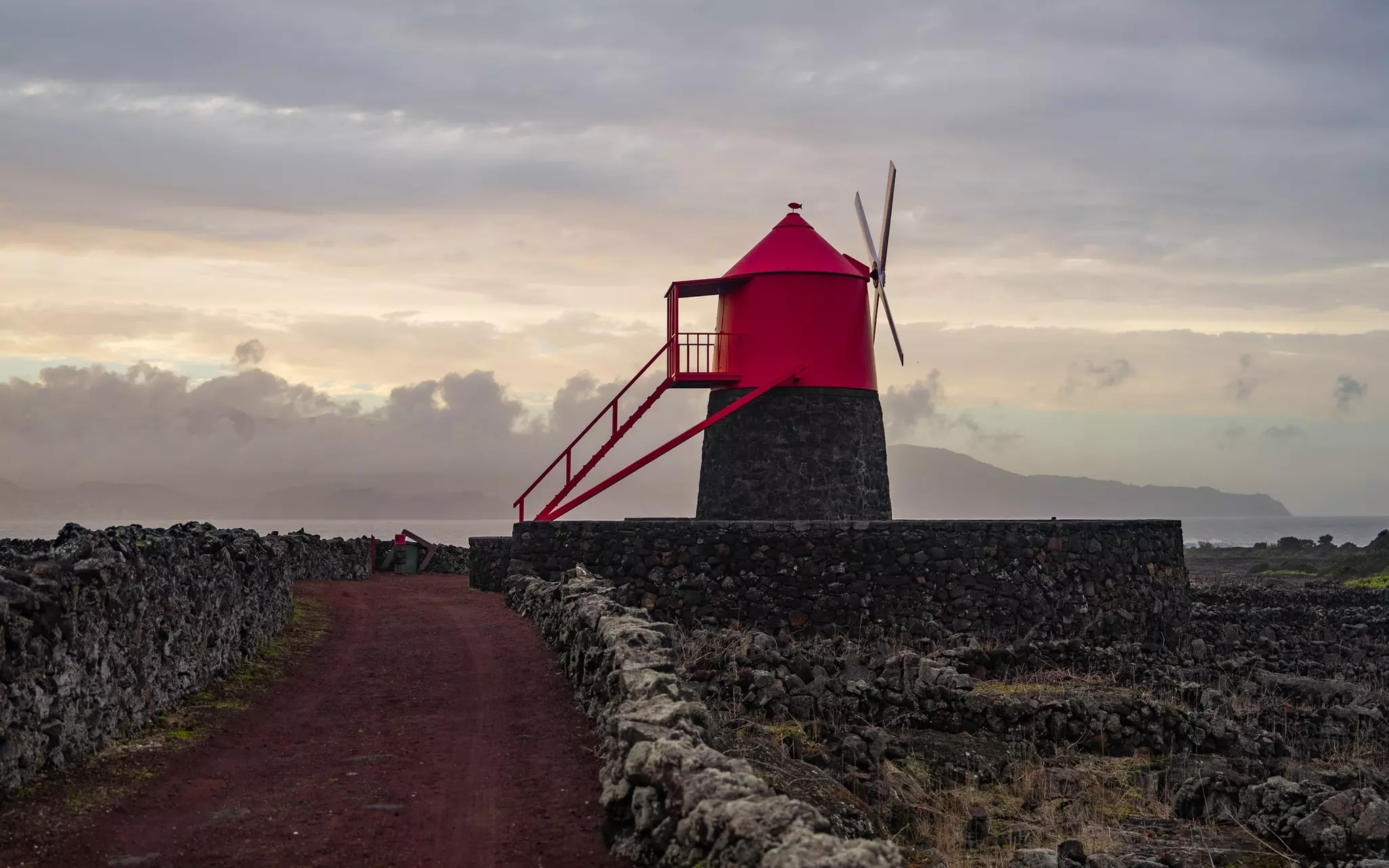 Red dirt path bordered by low stone walls leading to a red-topped windmill.