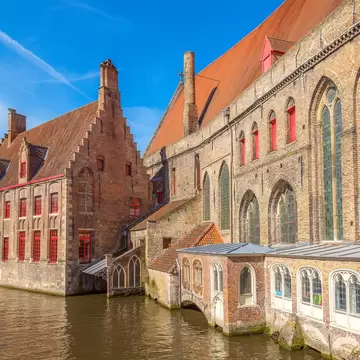 Stepped-gable brick hospital buildings with red window frames and tall Gothic windows rising straight from a canal in Bruges