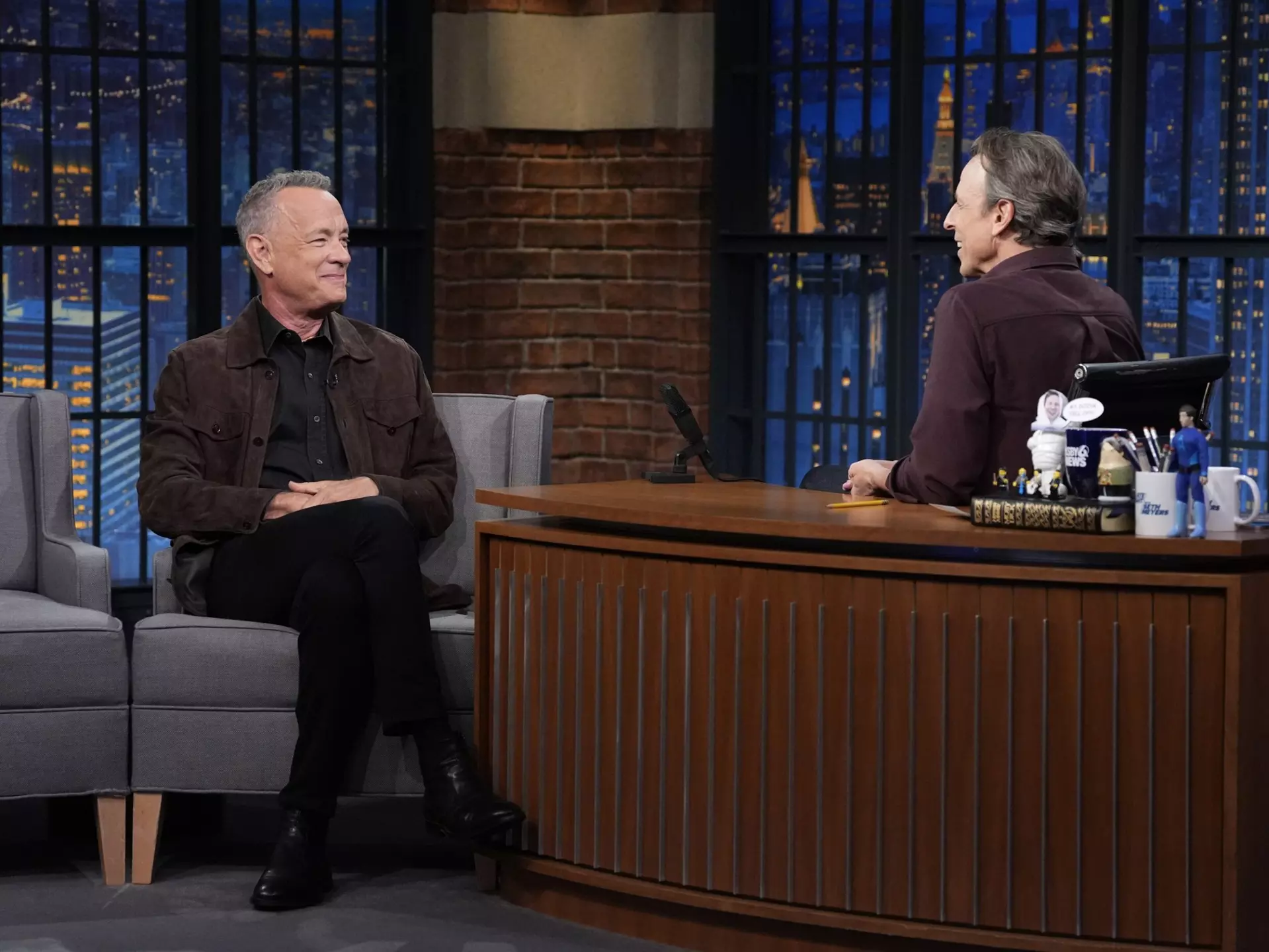 Two men sit in a TV studio in discussion. One is actor Tom Hanks, the other is the host, Seth Meyers
