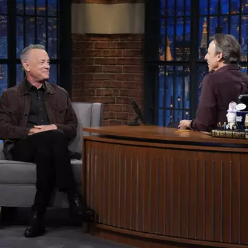 Two men sit in a TV studio in discussion. One is actor Tom Hanks, the other is the host, Seth Meyers