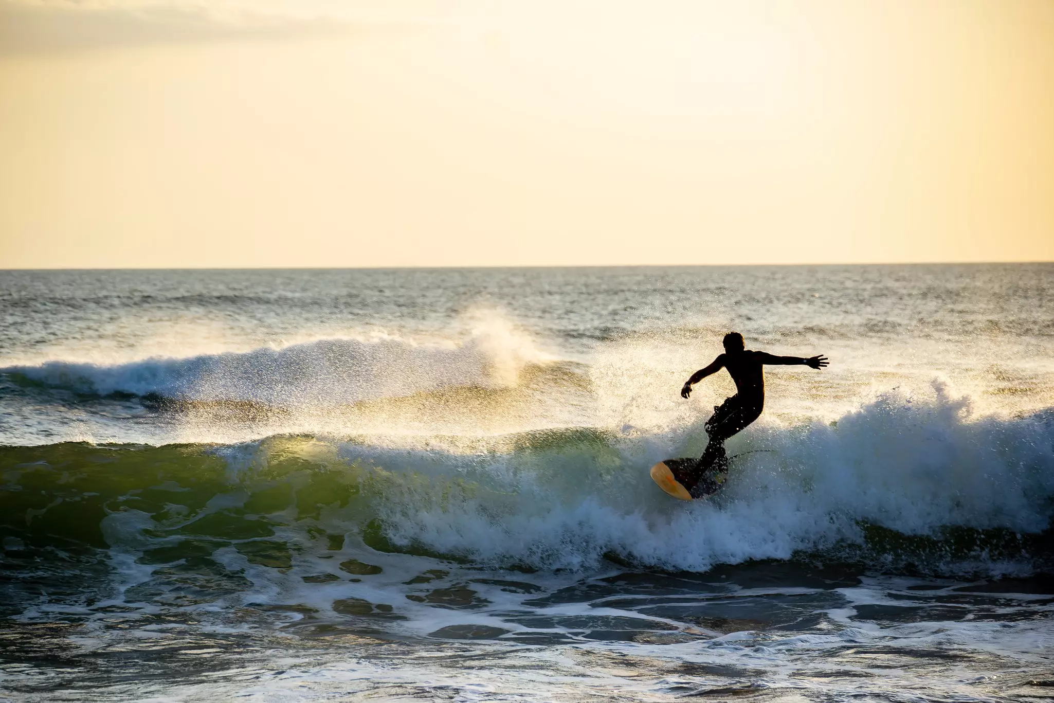 A surfer silhouetted against the sunset at Kedungu Beach in Bali, Indonesia.