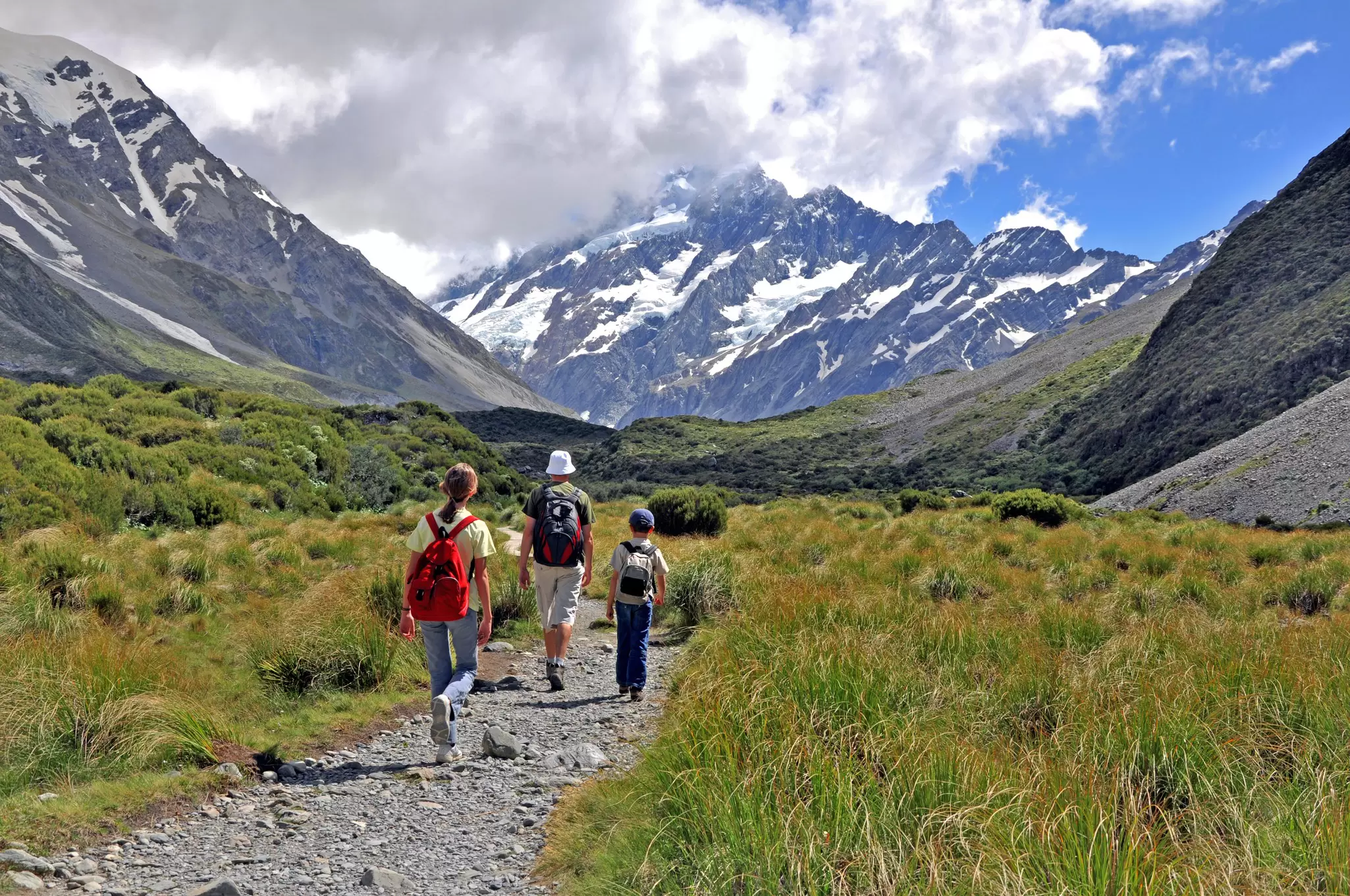 Two adults and a child walking along a rocky path towards a mountain.