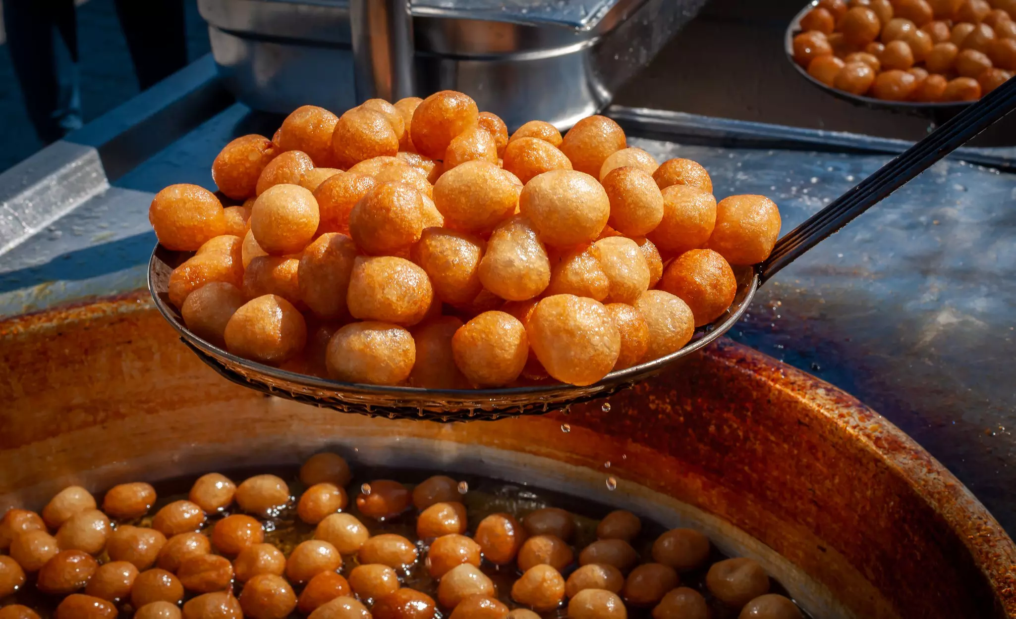 Freshly fried Lokma (luqma - arabic) piled high on a large spoon straight from the deep fat fryer; a popular middle eastern dessert of small dough balls deep fried then coated in sugar or honey syrup