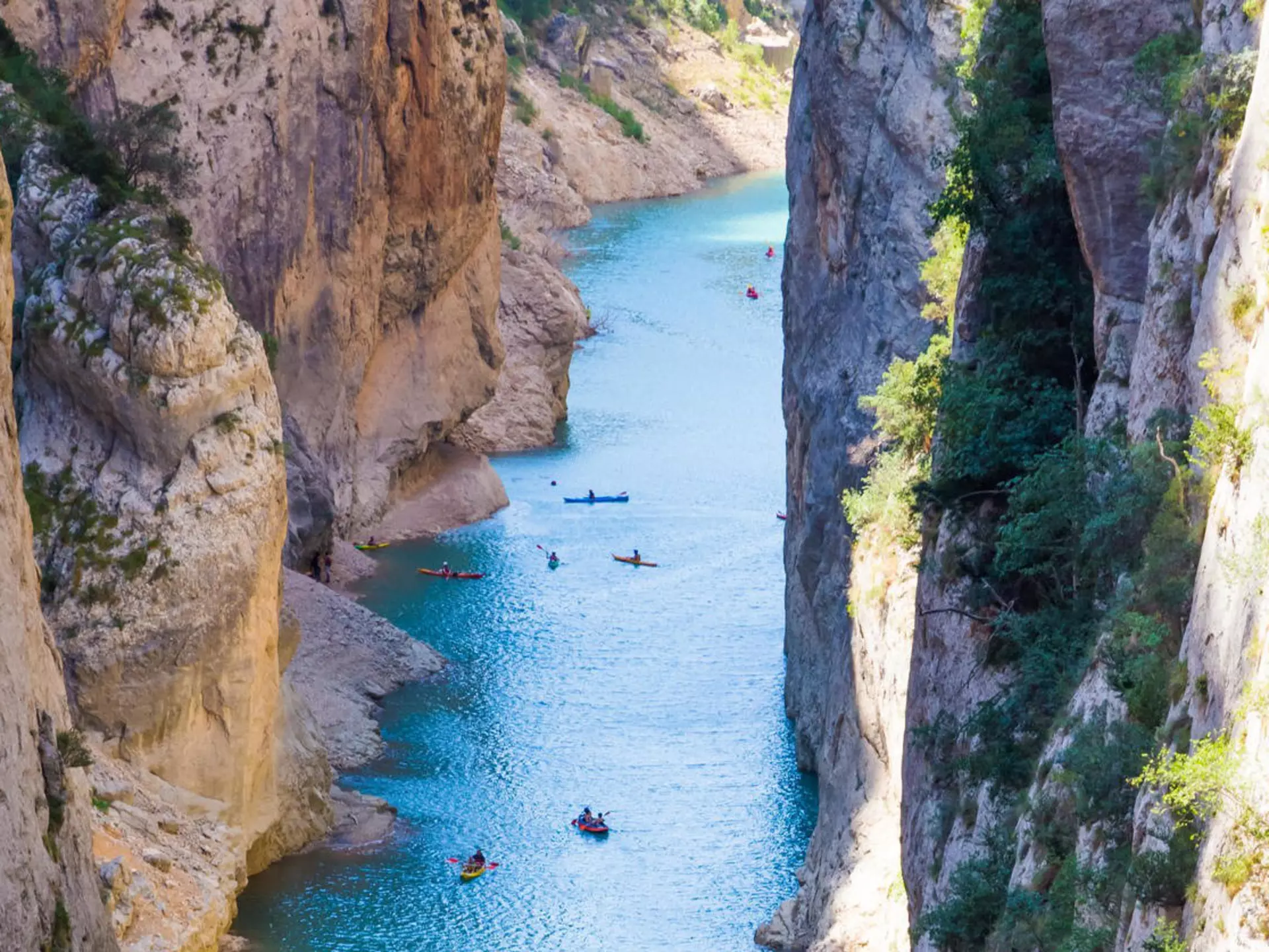 Kayakers paddle through blue water in a deep gorge.