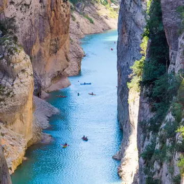 Kayakers paddle through blue water in a deep gorge.