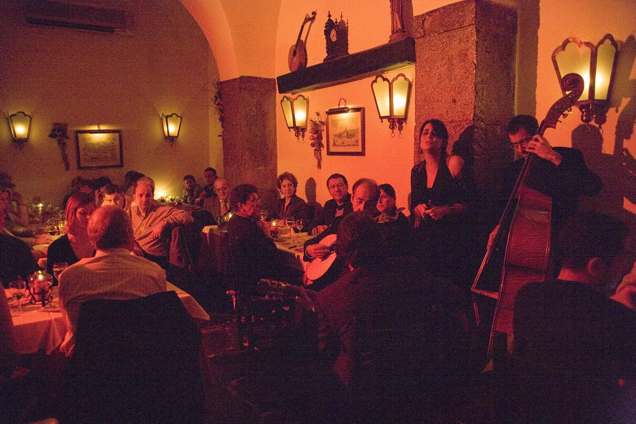 Musicians perform for a packed small room of spectators. The scene is lit atmospherically.