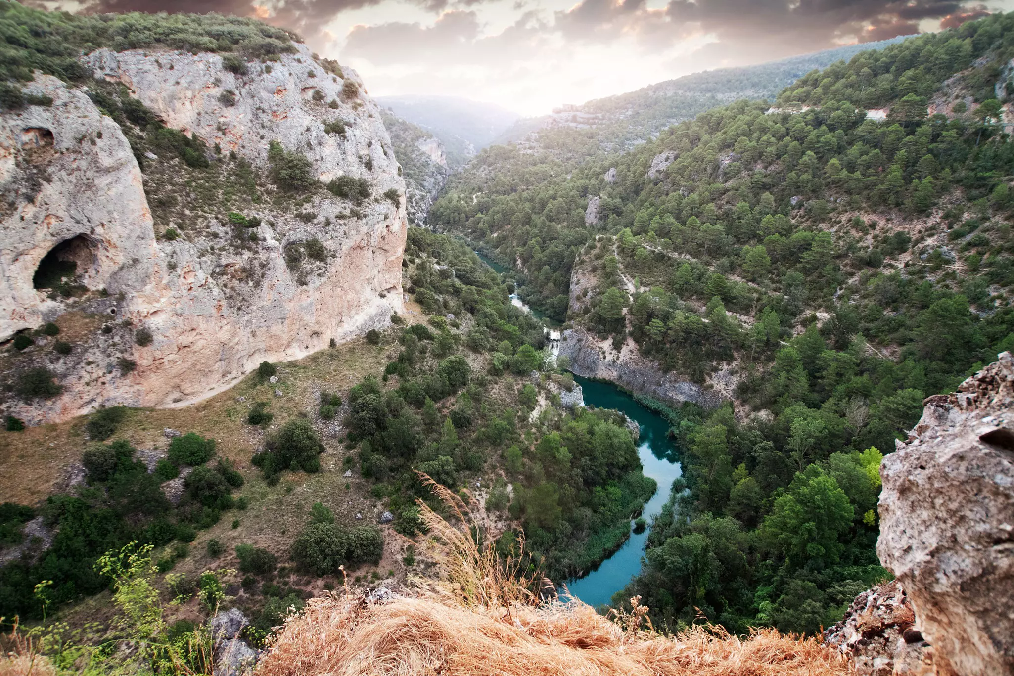 View from a cliff top of the Río Júca cutting through the Ventano del Diablo canyon with a hazy sky above.