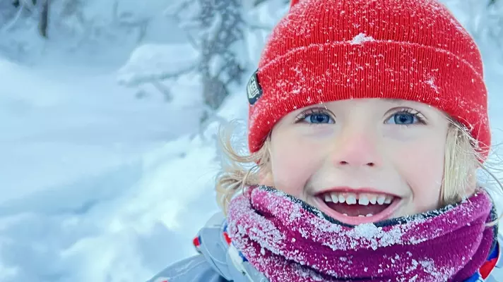 A boy wearing a red hat smiles in a snowy landscape in Fairbanks, Alaska.