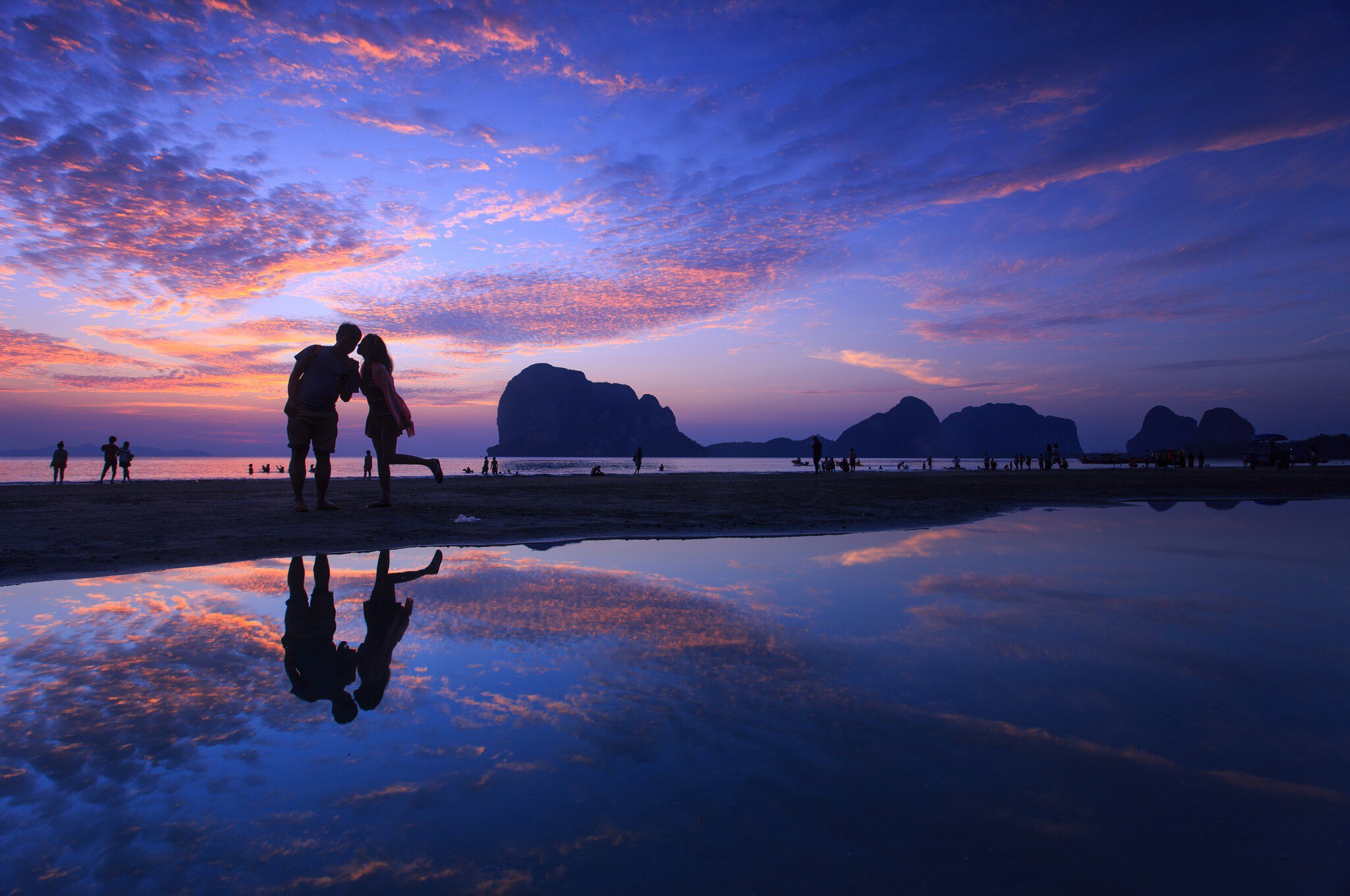 Silhouette of kissing couple and people on beach at sunset.