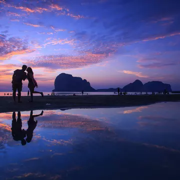Silhouette of kissing couple and people on beach at sunset.
