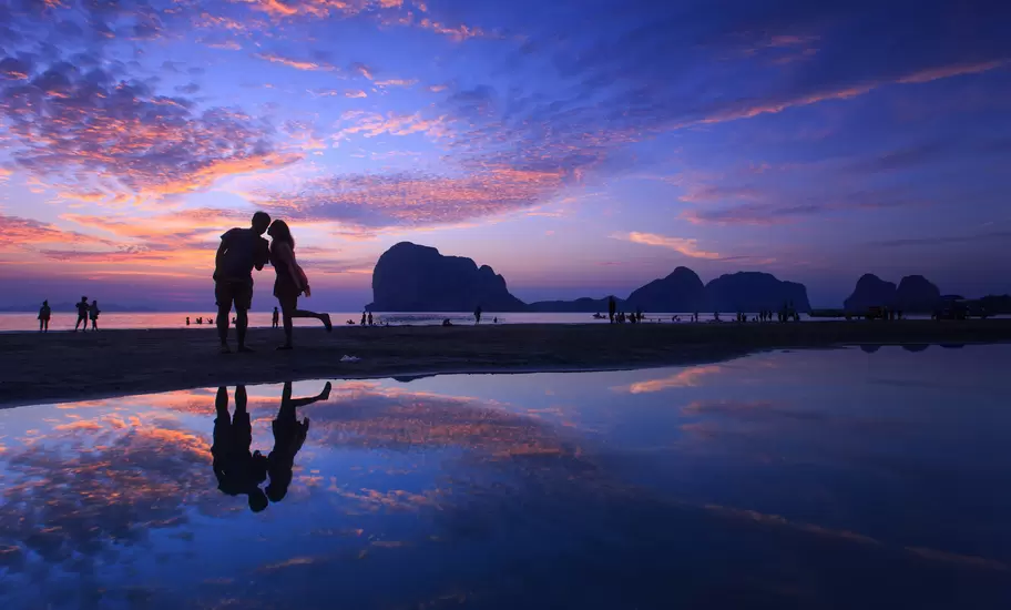 Silhouette of kissing couple and people on beach at sunset.