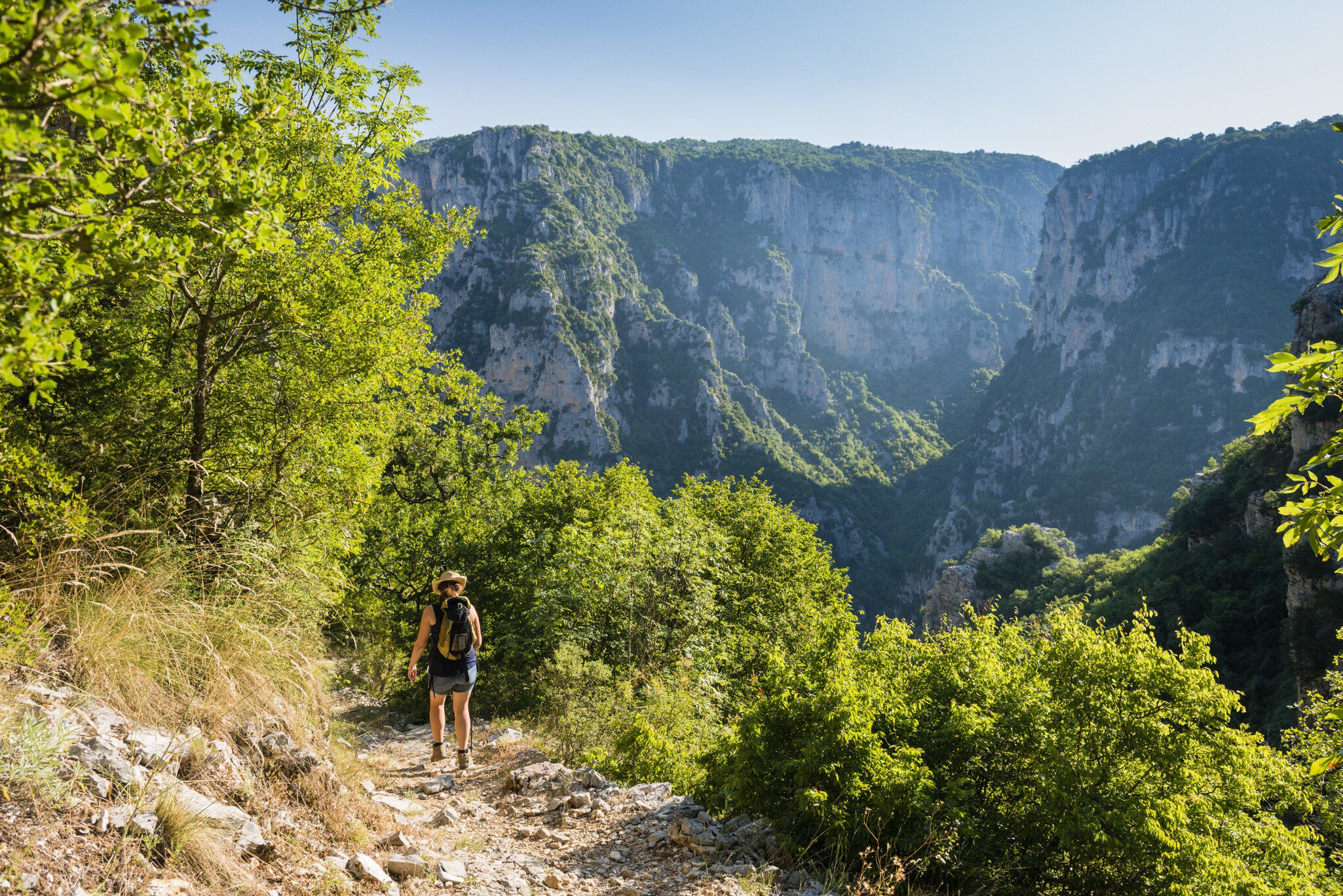 A woman follows an uneven rocky hiking trail down into a gorge.