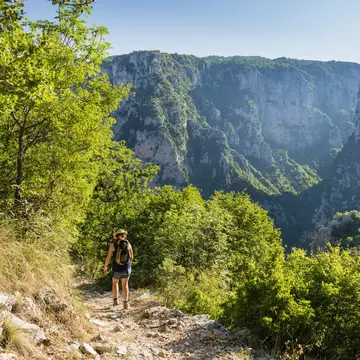A woman follows an uneven rocky hiking trail down into a gorge.