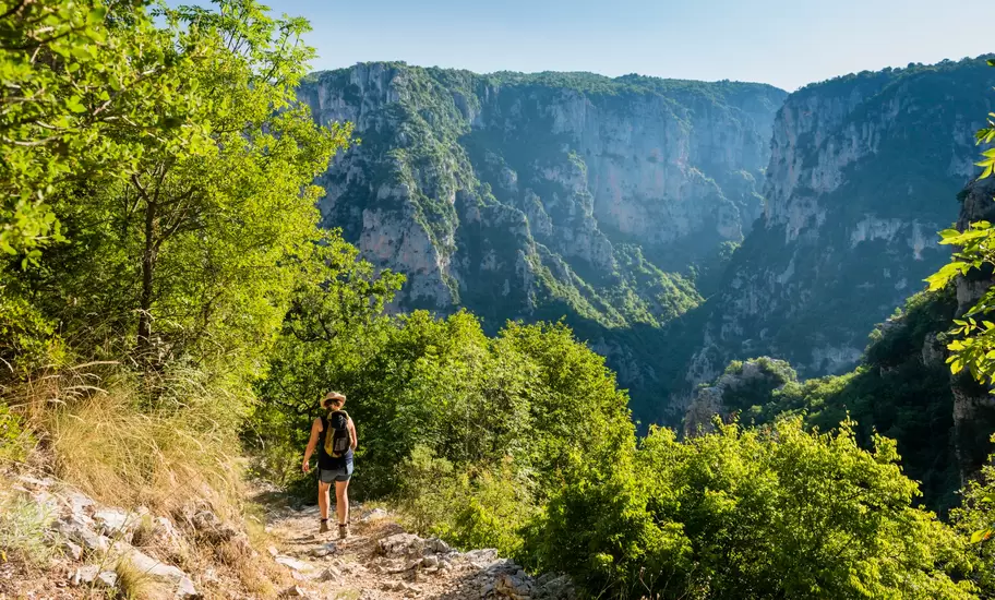 A woman follows an uneven rocky hiking trail down into a gorge.