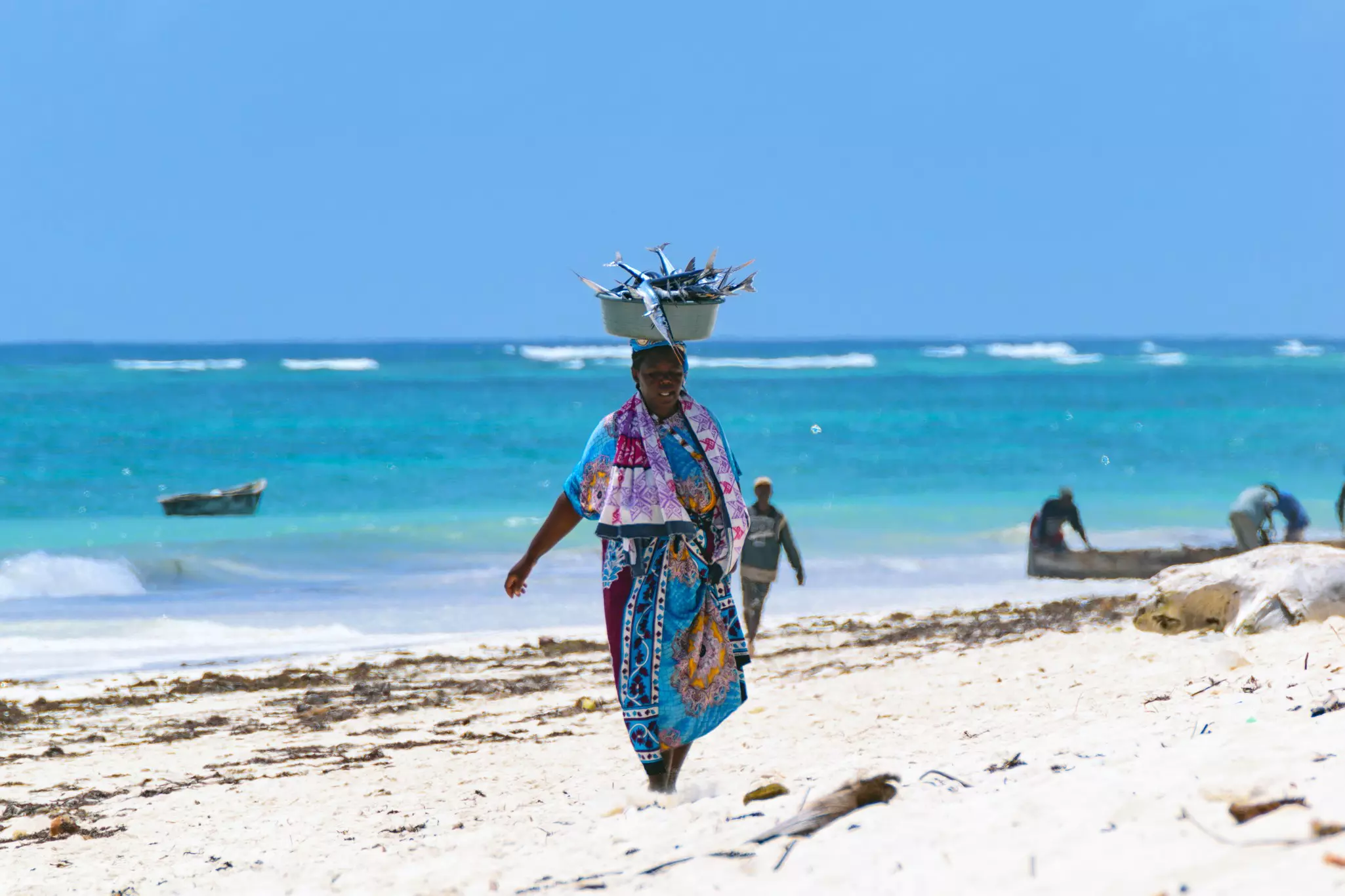 Woman walking with a basket of fish balanced on her head on Diani Beach, Mombasa, Kenya.