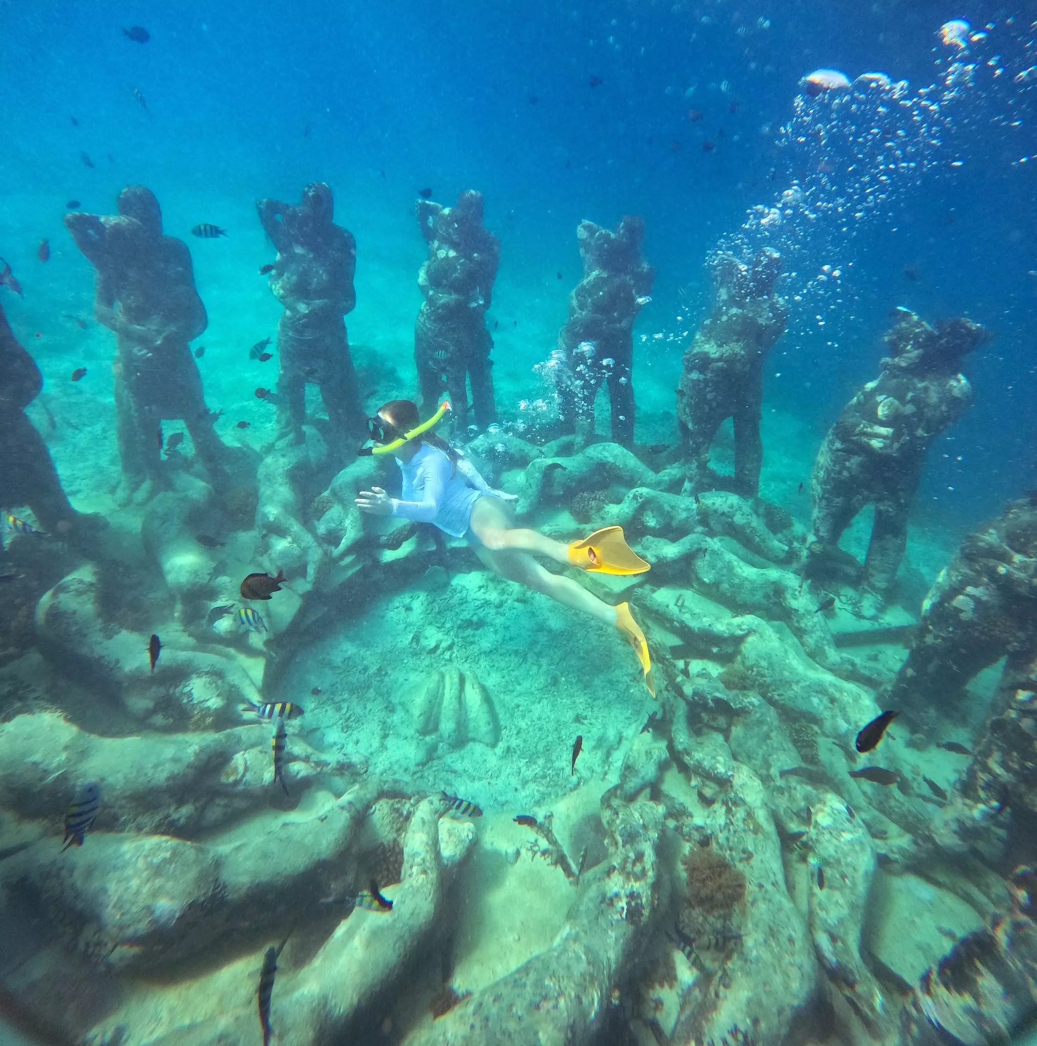 A woman snorkels near underwater sculptures of couples embraced and people lying on the ocean floor