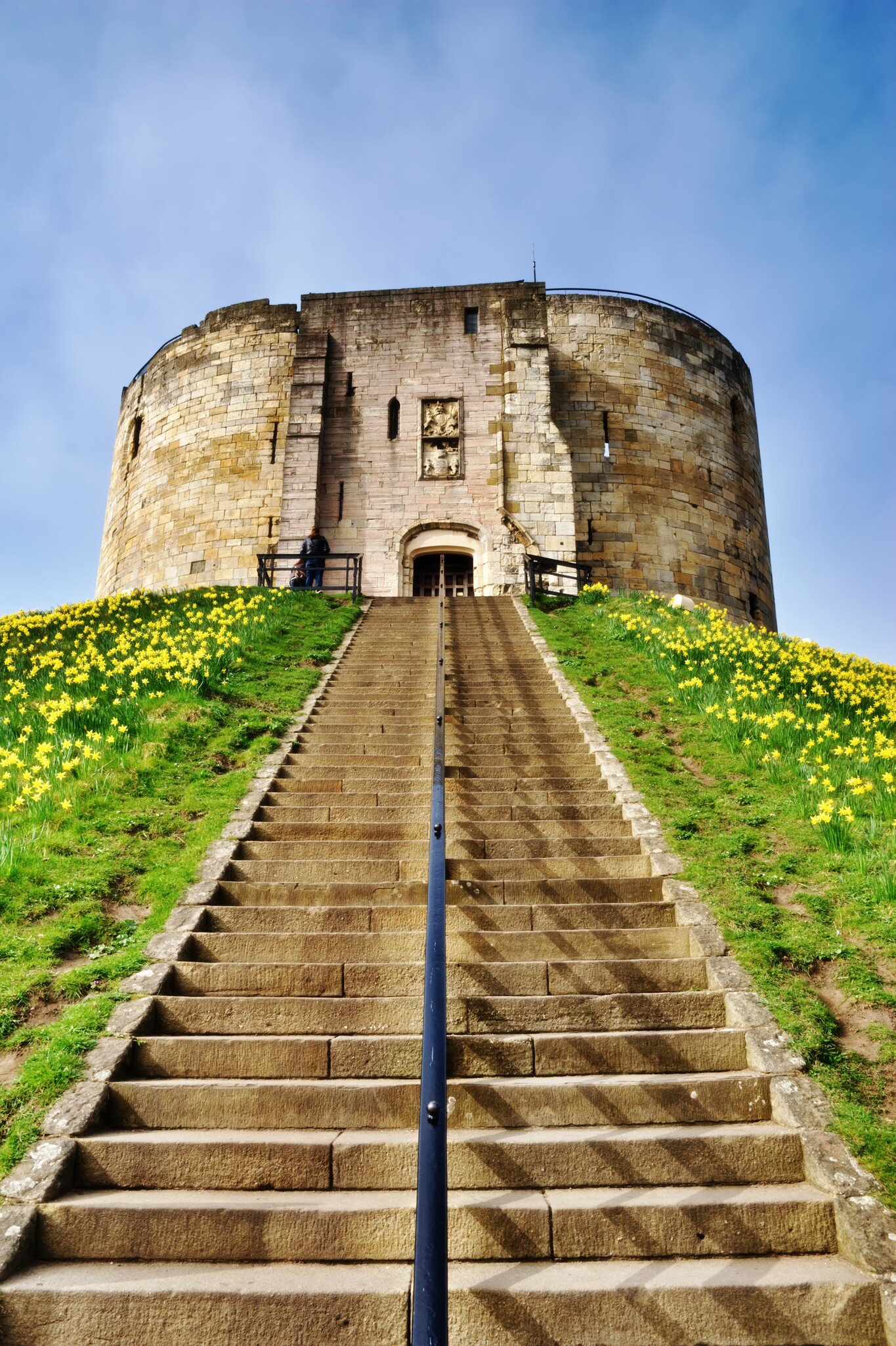 York, United Kingdom - October 2, 2016: View of Clifford's Tower, a Norman Motte and Bailey castle in York, England, with visitors climbing the steps to see the attraction.