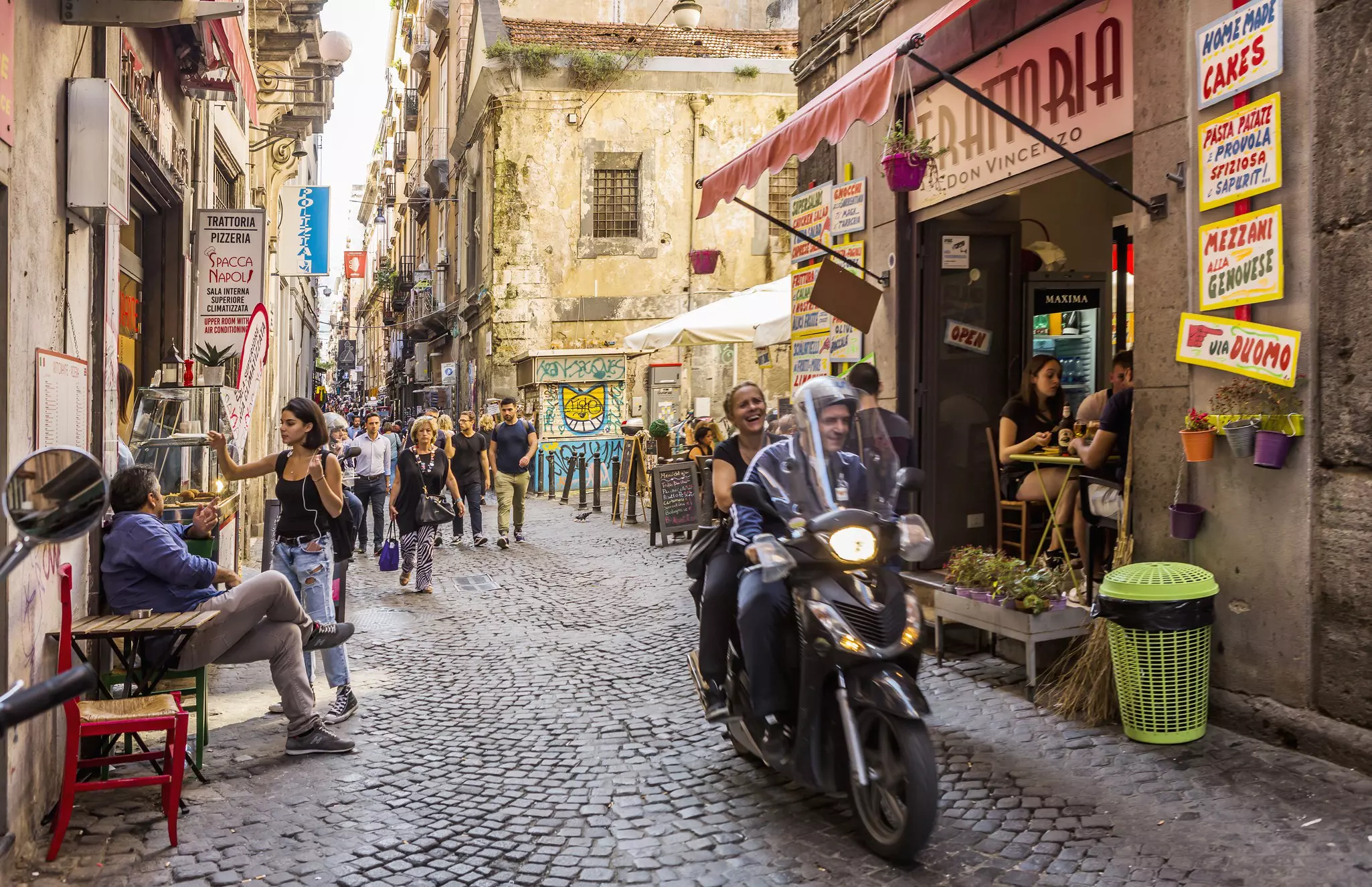 People ride a scooter on a narrow street in Italy.