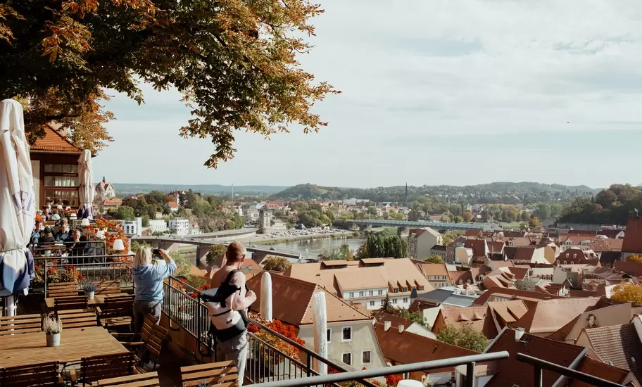 Visitors on a café terrace look out over red-tiled rooftops, Elbe bridges and wooded hills in Saxony