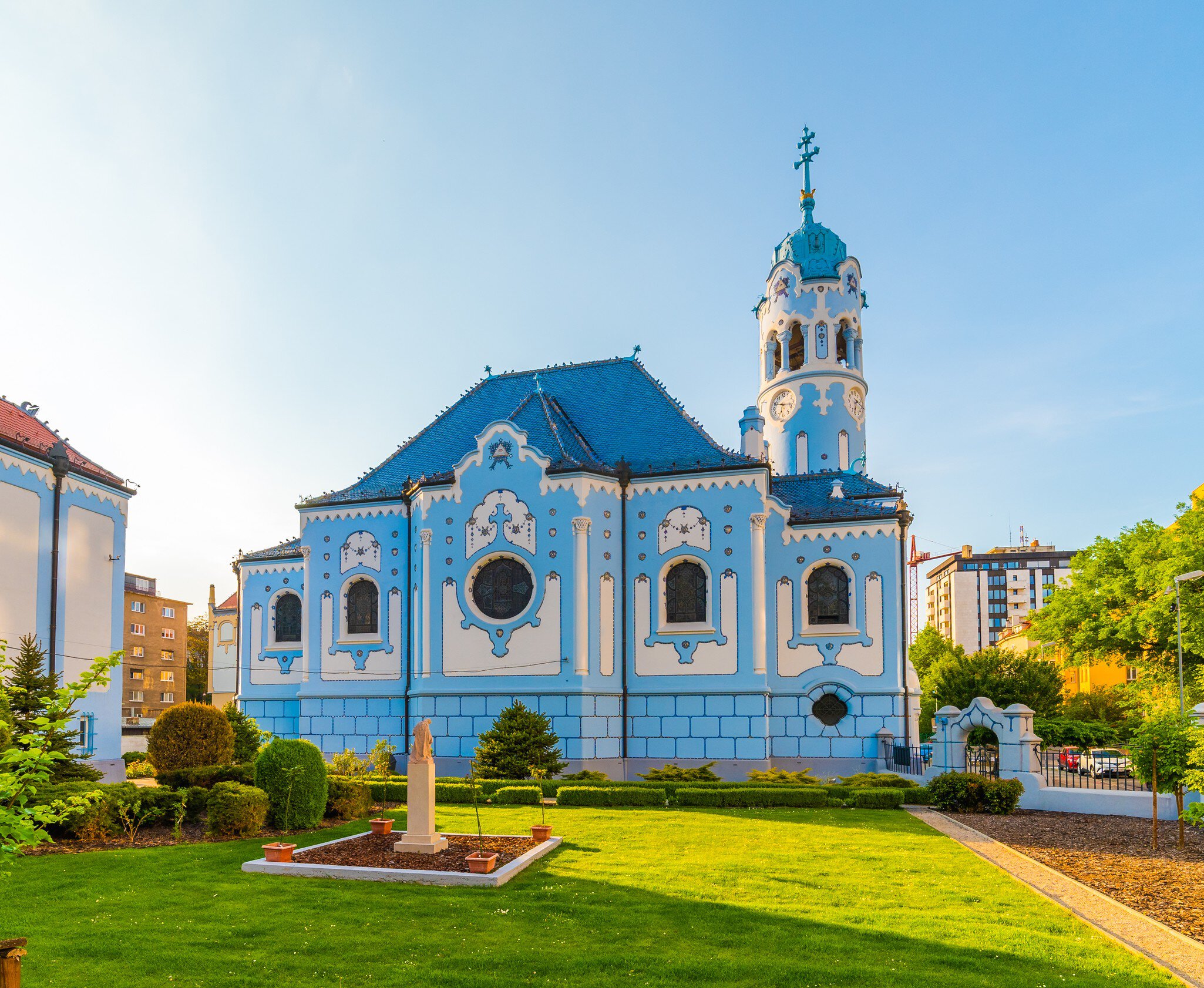 Powder-blue church with ornate white trim, a blue tiled roof and a round clock tower beside a lawn.