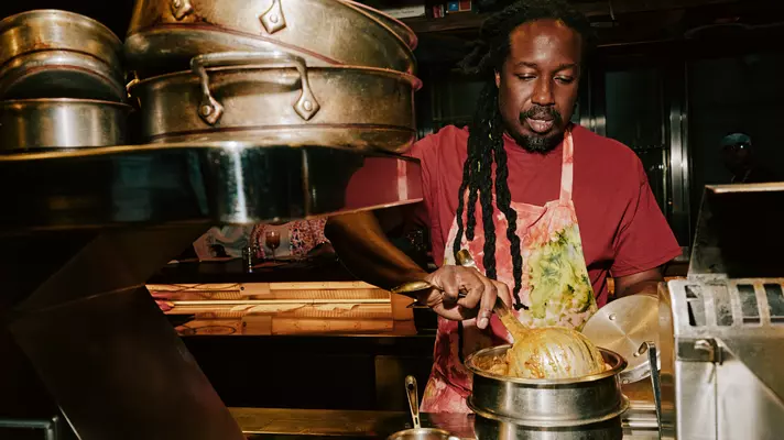 A man in a red T-shirt and tie-dye apron working in a restaurant kitchen.