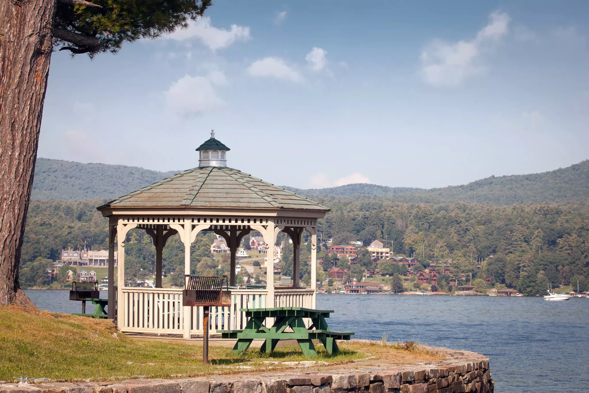 A white gazebo and a green picnic table by a lake.