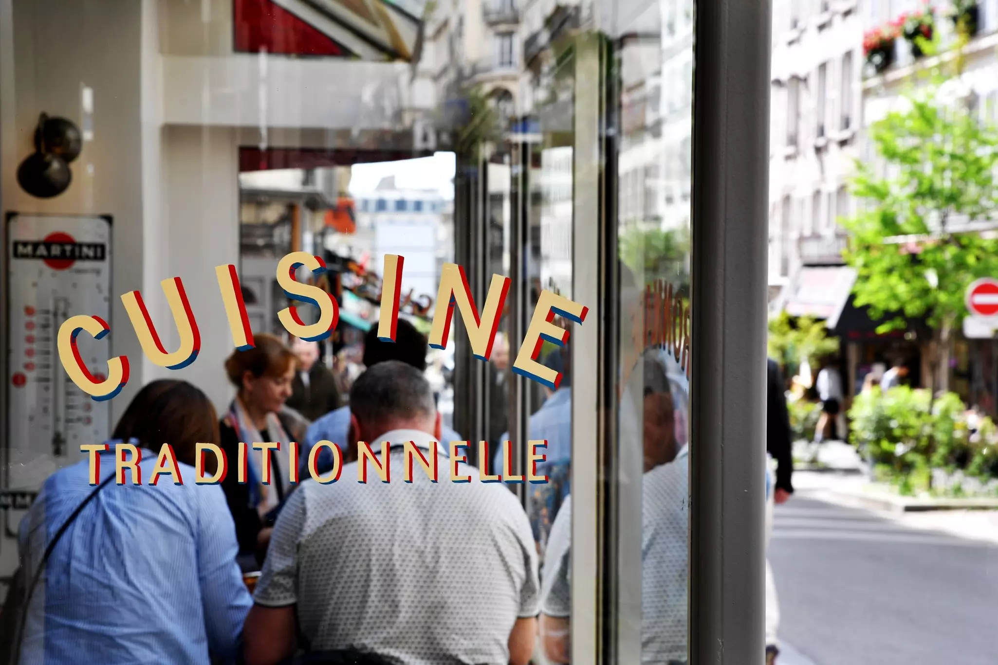 People sit in the window of a restaurant with a sign that says "cuisine traditionnelle".