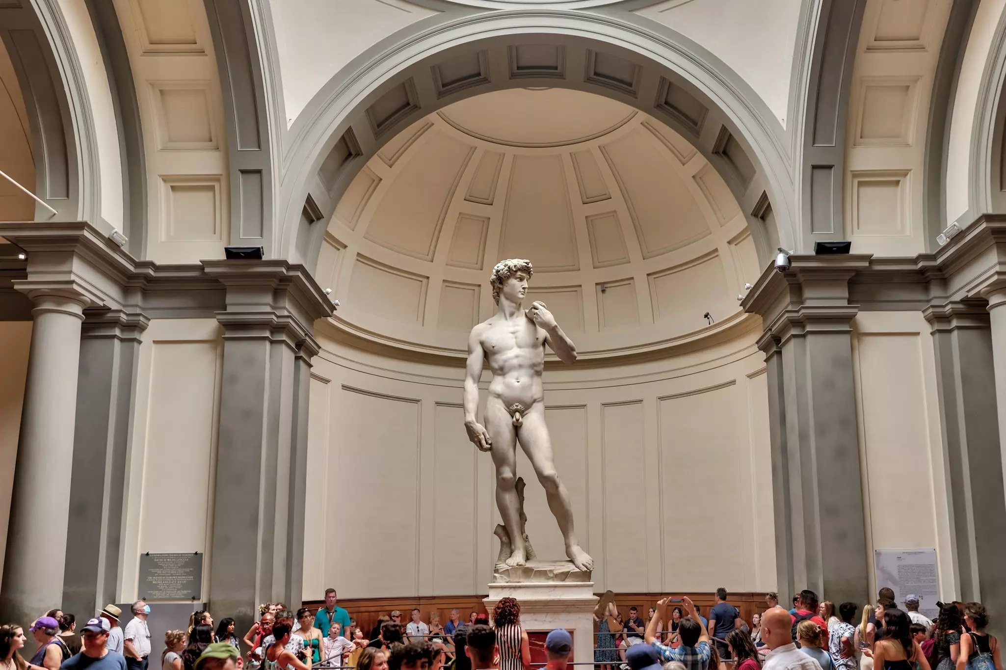 People in a gallery take photos of the marble statue of David