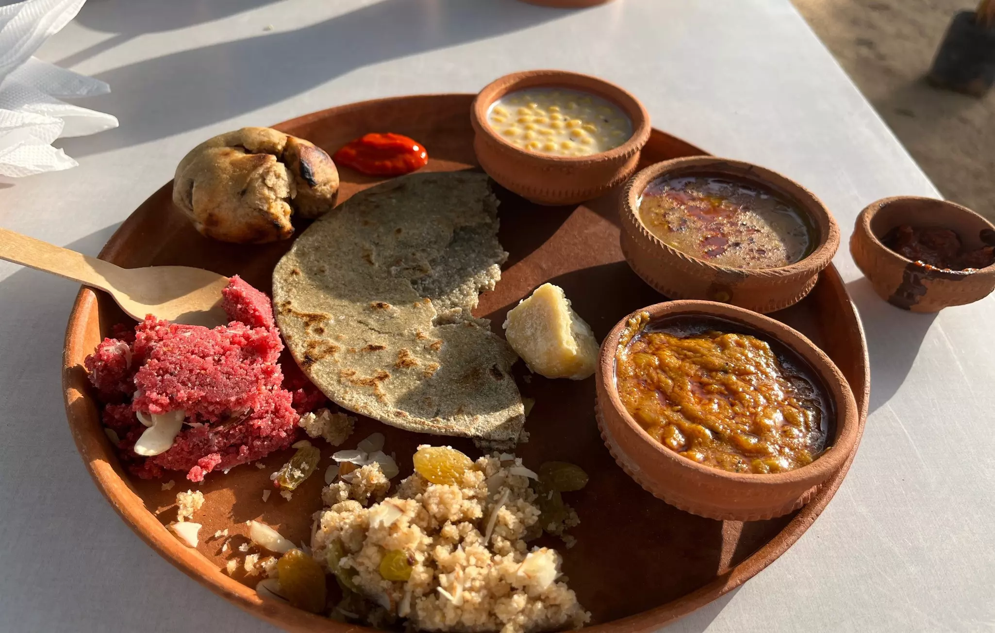 Three bowls with different dishes on a plate with bread and other food items.