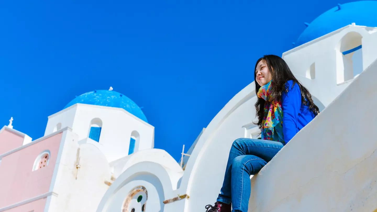 A woman sitting on the edge of a rooftop in Oia town and enjoying the view of Santorini.