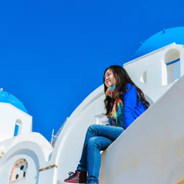 A woman sitting on the edge of a rooftop in Oia town and enjoying the view of Santorini.