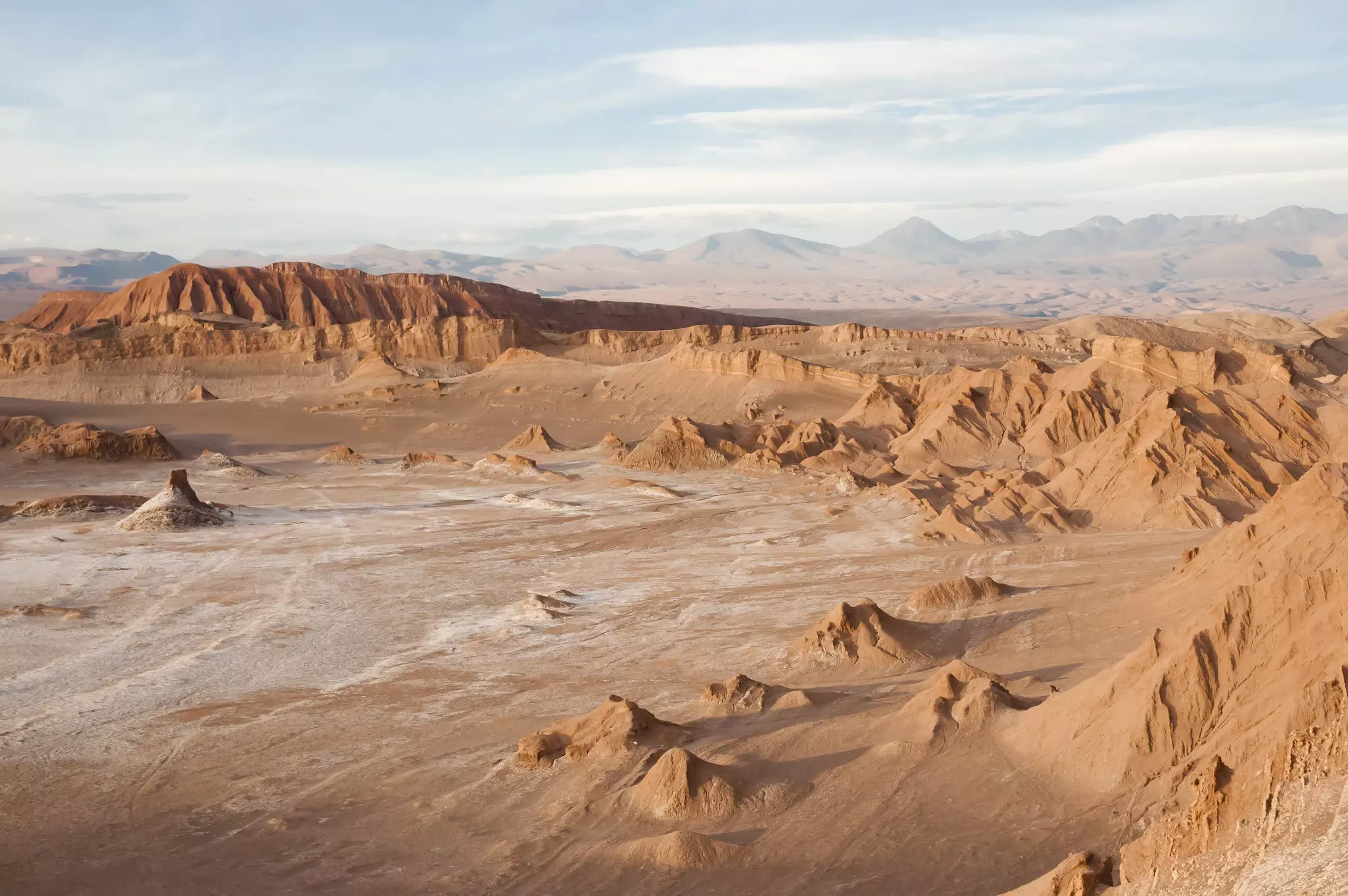 A barren landscape of slightly reddish sand with rock formations in peaks around the perimeter.