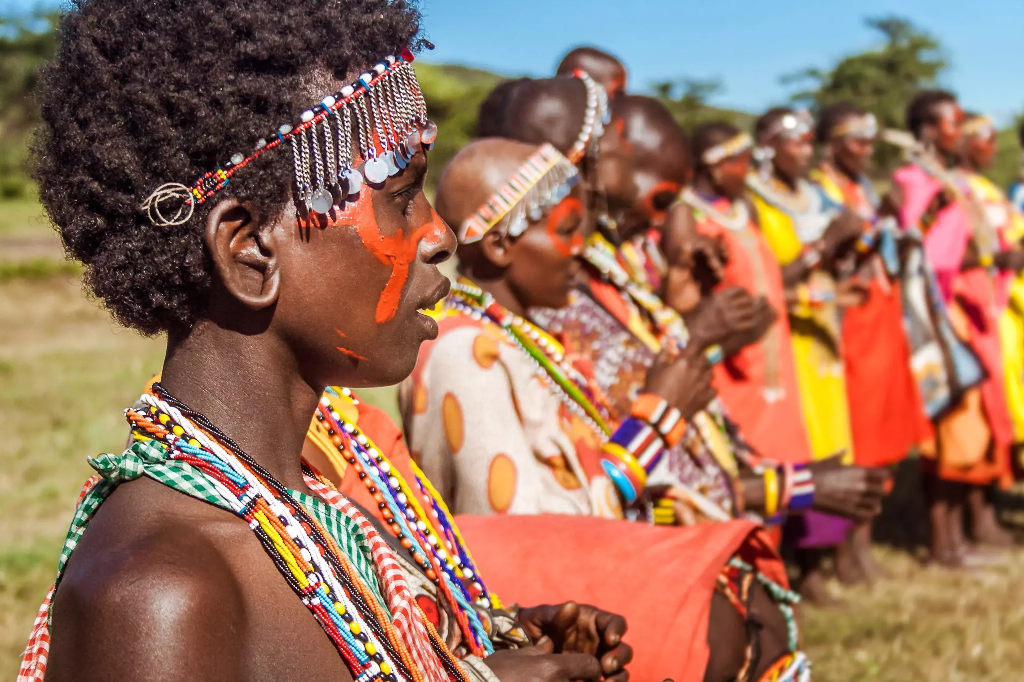 A row of women in colorful traditional clothing, beads and facepaint standing in a row.