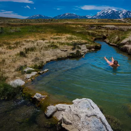 A person floats in a hot spring in a meadow.