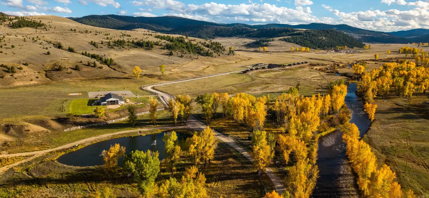 Aerial view of a barn next to a lake, surrounded by yellow fall foliage and mountains in the background