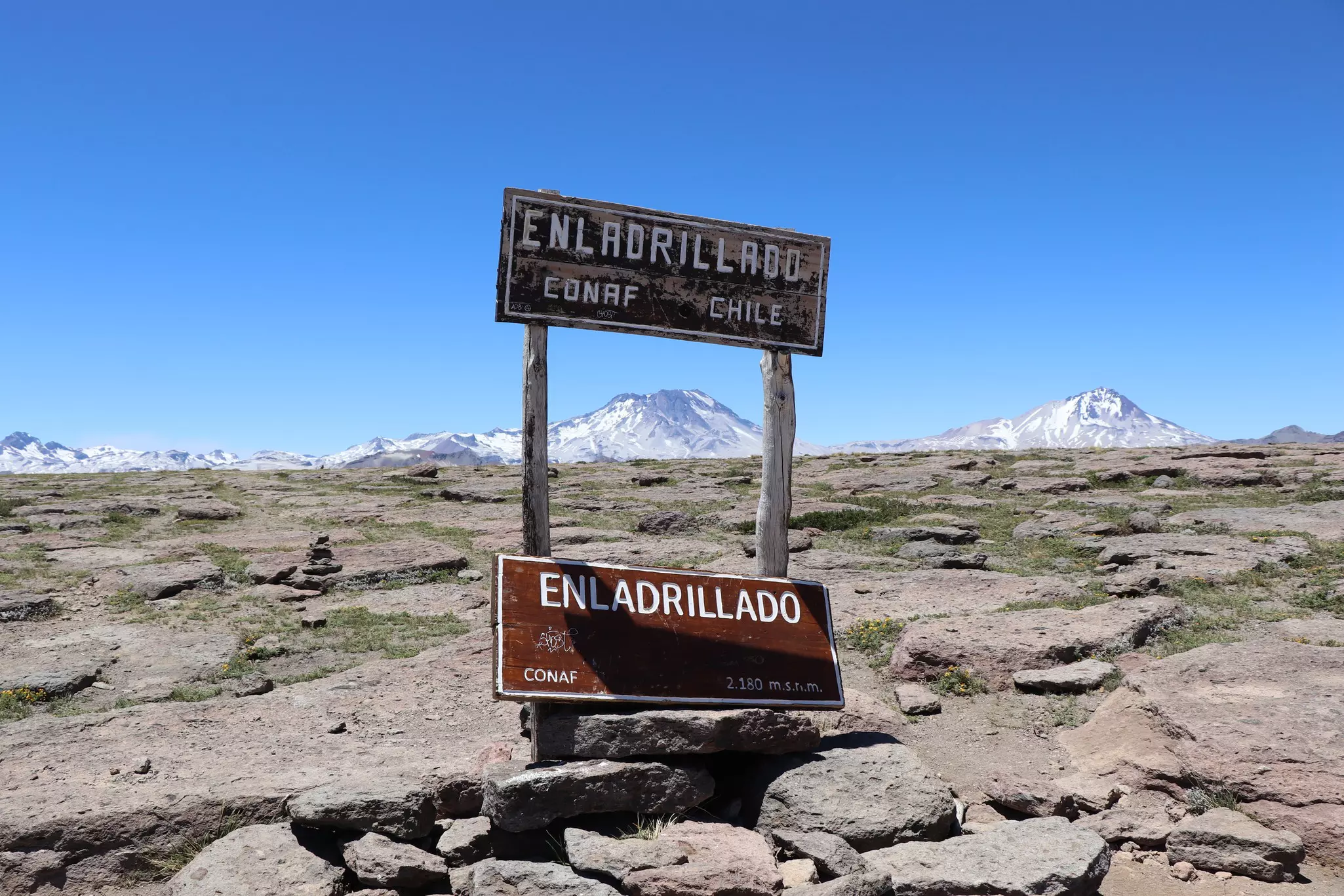 A sign on a high-altitude plateau of basalt rocks with mountains in the distance.