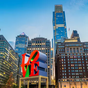 A large red sculpture spelling out "LOVE" in the center of a city square with high-rise buidlings all around