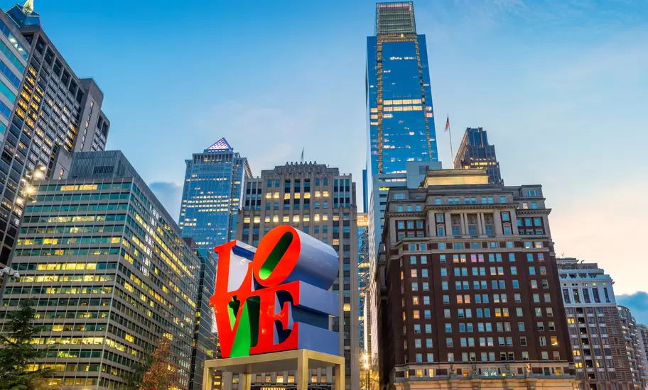 A large red sculpture spelling out "LOVE" in the center of a city square with high-rise buidlings all around