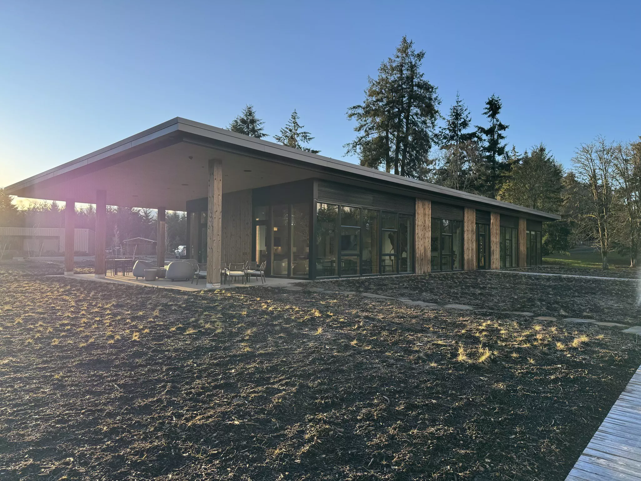The exterior of a modern, flat-roofed building with floor-to-ceiling windows with a winter-barren lawn in front and trees in the distance on a sunny day.