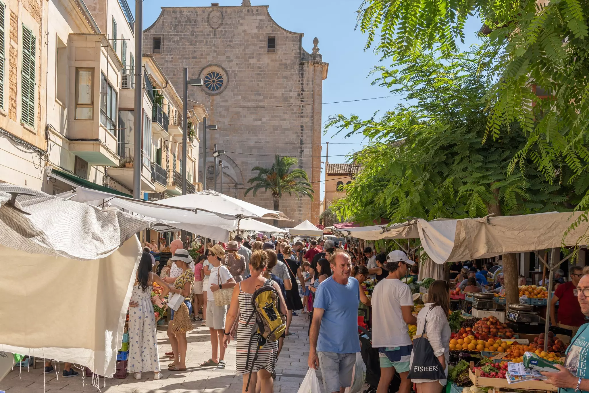 People purchase items at a street market with stalls selling fresh produce.