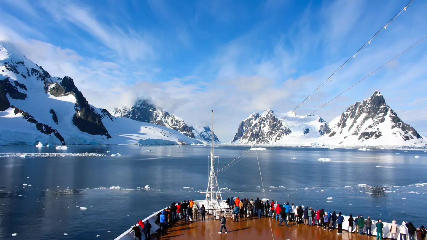 Passengers on deck on a cruise ship passing a rocky coastline in the Antarctic Peninsula.