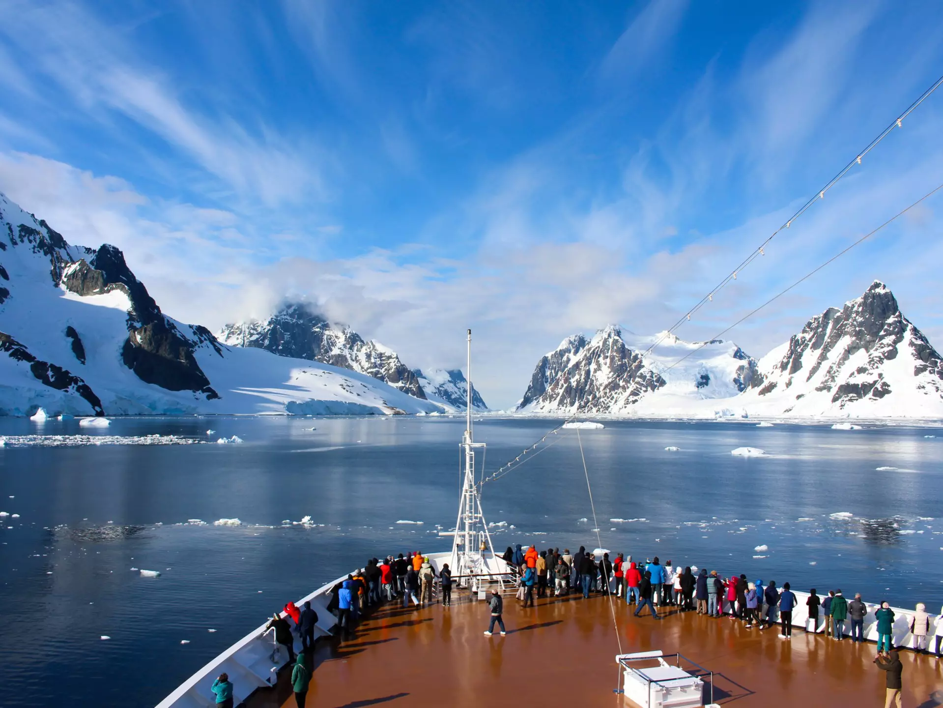 Passengers on deck on a cruise ship passing a rocky coastline in the Antarctic Peninsula.