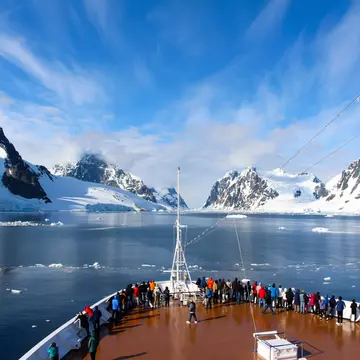 Passengers on deck on a cruise ship passing a rocky coastline in the Antarctic Peninsula.